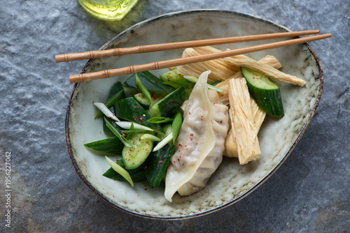 Smashed cucumber and tofu skin salad with steamed pork dumpling, horizontal shot on a dark-grey granite background