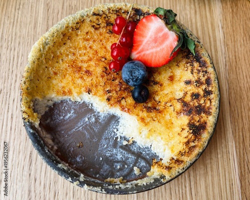 Homemade crème brûlée with crispy caramel top, decorated with strawberry, blueberries, and red currants, minimal food styling.