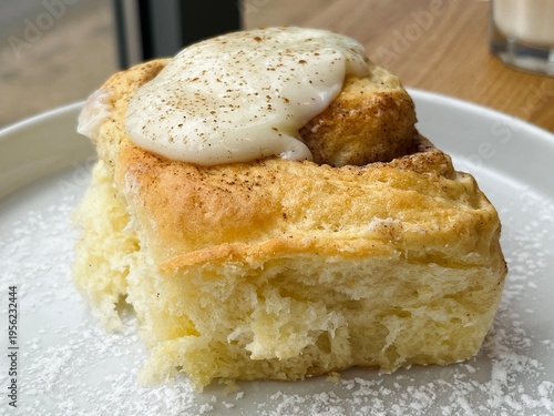 Close-up of a sweet cinnamon bun topped with glaze, served on a minimal plate with powdered sugar.