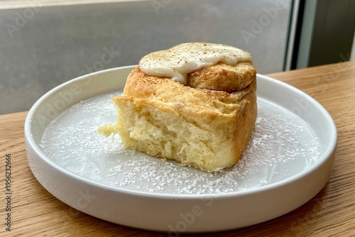 Tasty cinnamon roll with creamy glaze, powdered sugar on plate, homemade bakery concept.