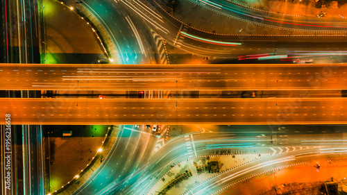Top view aerial shot of symmetrical highway interchange at night, glowing orange traffic streams crossing smooth curved roads, captured with high angle and neon lighting, representing modern transport