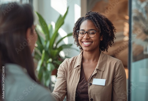 smiling professional woman wearing glasses warmly greeting a client with a handshake in a modern office environment conveying confidence trust and positive business interaction