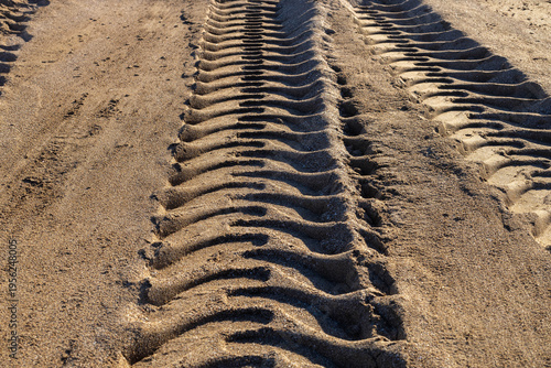 Heavy tire tracks on a sandy beach from coastal maintenance machinery. Preparation of the shoreline for the tourist season and cleaning after winter storms. Industrial texture on sand.