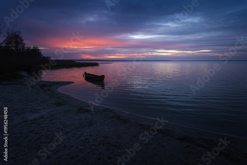 Sunset on the lake. Old rural wooden, fishing boat moored in the shallow waters of the lake. Fragment. DOF