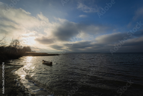 Old rural wooden, fishing boat is moored on the shore of a lake. A gloomy windy day