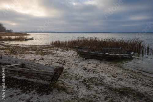Old rural wooden, fishing boat is moored on the shore of a lake. A gloomy windy day