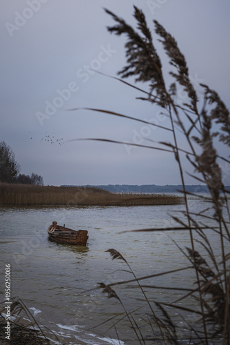 Old rural wooden, fishing boat is moored on the shore of a lake. A gloomy foggy day
