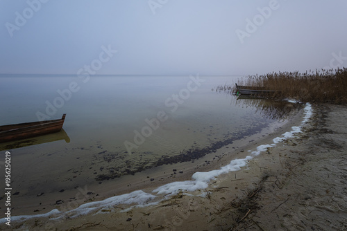 Old rural wooden, fishing boat is moored on the shore of a lake. A gloomy foggy day