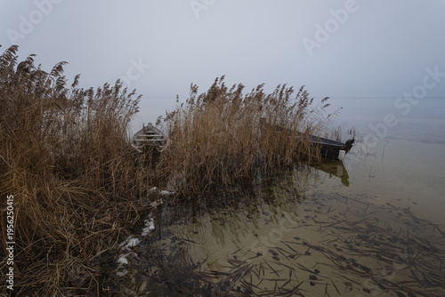 Old rural wooden, fishing boat is moored on the shore of a lake. A gloomy foggy day