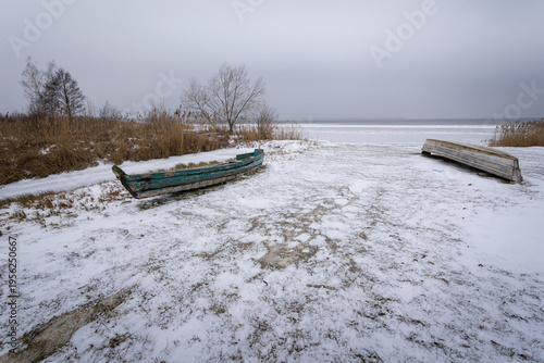 Old wooden boats on the shore of a snowy and frozen lake