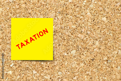 Yellow note paper with word taxation on cork board background with copy space