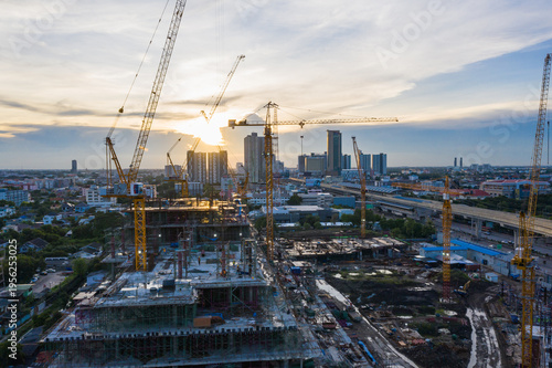 Wide-angle panoramic view of large construction project with cranes and unfinished buildings during sunset in metropolitan area, symbolizing engineering progress, real estate investment,