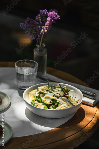 Foto Light green salad with shaved zucchini pine nuts and herbs served in white bowl