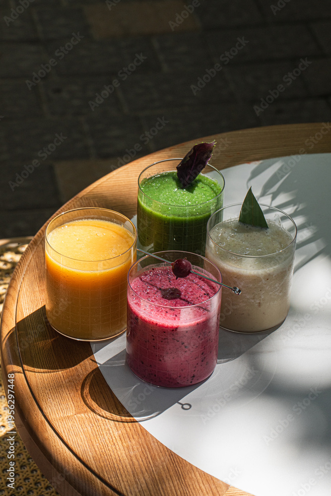 Fototapeta premium Variety of fresh fruit and vegetable smoothies served in glass cups on table in cafe setting