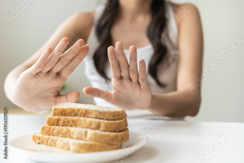 Gluten allergy, asian young woman hand push out, refusing to eat white bread slice on plate in breakfast food meal at home, girl having a stomach ache. Gluten intolerant and Gluten free diet concept.