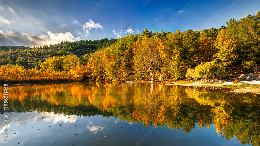 Obraz premium Thasos island, North Greece, Dam Maries. Lake reflecting vibrant autumn colors with hills and blue sky.