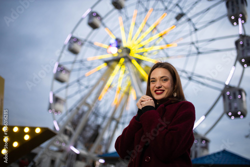 A woman in an amusement park with a Ferris wheel in the background on a summer evening