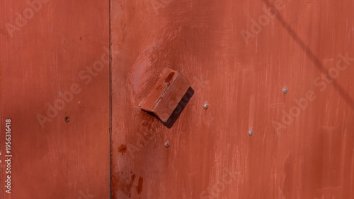 Close-up of a weathered red metal garage door with a welded handle and visible bolts.