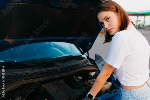 A female driver with an open hood in a parking lot, a car breakdown on the road in summer