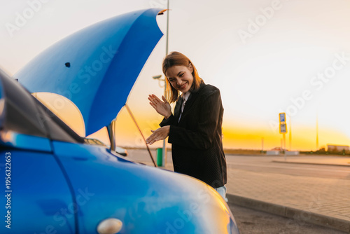 A female driver with an open hood in a parking lot, a car breakdown on the road in summer