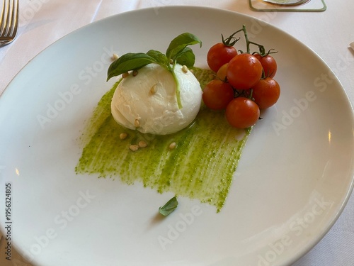 Burrata mit Tomaten und grünem Pesto auf Teller, modern angerichtet, frisches Vorspeisengericht im Restaurant, stilvolle Foodaufnahme mit Copyspace