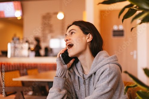 Schilderij op canvas Happy young woman talking on smartphone in cafe and laughing loudly, cheerful gi