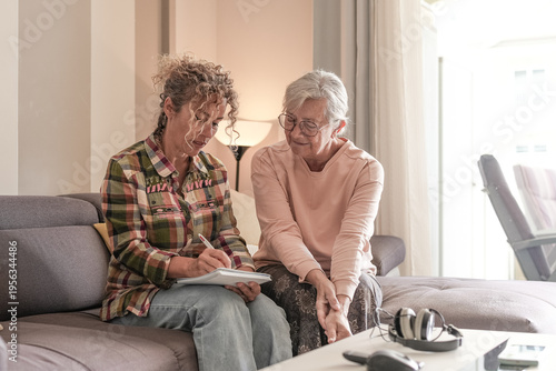 Smiling Senior woman and Caregiver Sharing a Moment sitting together on sofa at home. Concept of assistance and help to our elderly