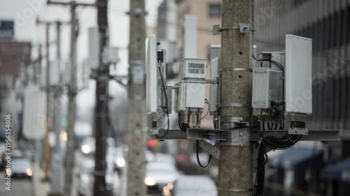 Cluster of small microcell devices aligned on utility poles overhead in a dense urban passage foremost unit sharply captured against a blurred street scene.