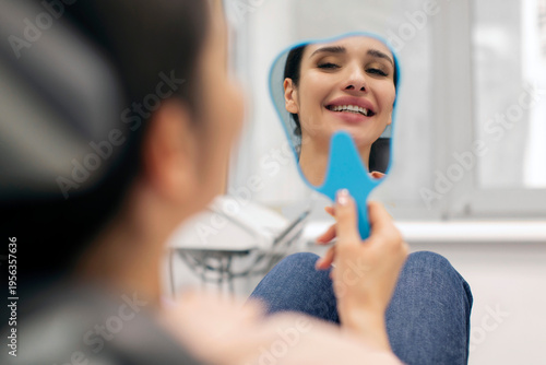 Fotografija Happy woman looking at her reflection in small mirror after having dental treatm