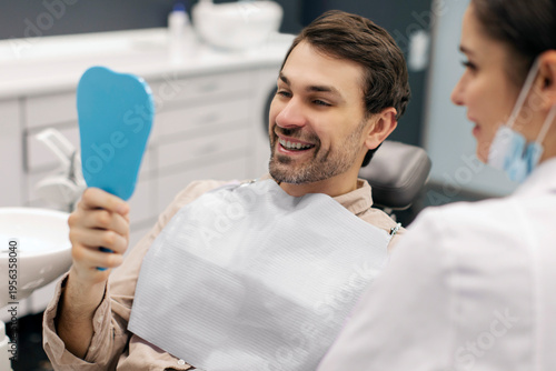 Canvas Print Happy male patient smiling while looking in mirror during dental appointment at