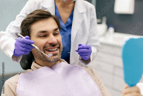 Фотография Man patient looking at mirror while dentist pointing at his teeth with tools and