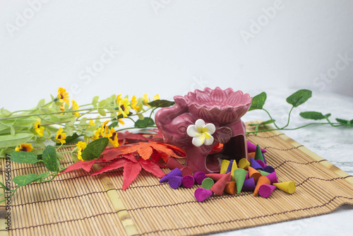 Still life composition with aromatherapy incense cones, essential oils, oil burner and candle on bamboo mat, creating calm spa and relaxation atmosphere.