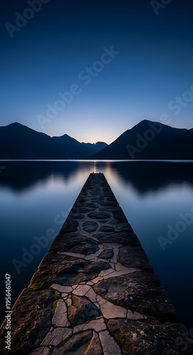 Serene stone pier leading to distant mountains across calm lake at twilight blue hour peaceful nature landscape