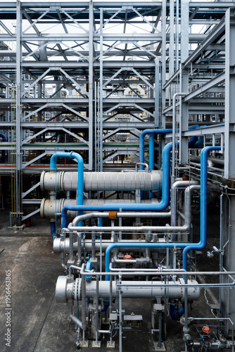 Industrial facility with complex piping and metal framework. Blue and silver pipes run through steel structures. Scene shows heavy machinery and construction details. Image fits engineering
