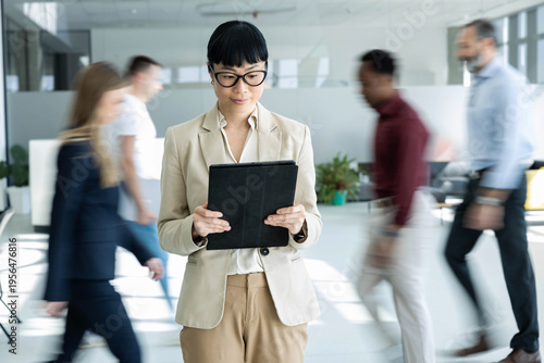 Photos Businesswoman standing with a digital tablet, managing tasks while other employe