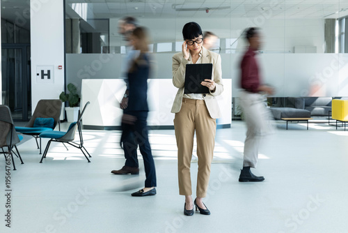 Bild auf Leinwand Professional businesswoman concentrating on her digital tablet in a busy, modern