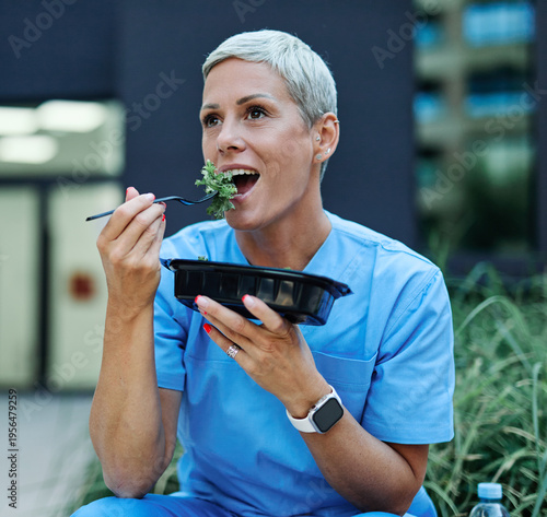 Young woman or a nurse or a doctor during office hours break enjoying a fresh salad in a park during a sunny day while smiling and relaxing on a bench