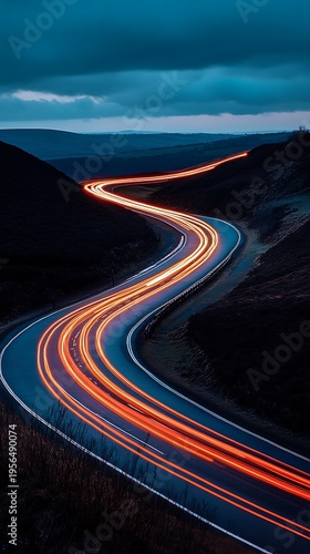 Traffic flowing through a dark landscape with a winding road at dusk or dawn