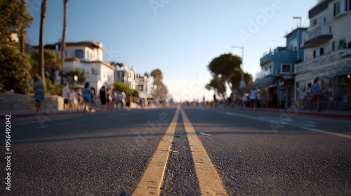 Perspective view down a sun drenched street in a vibrant coastal town with blurred buildings and people enjoying the day