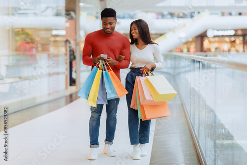 Obraz na płótnie A man and woman walk through a shopping mall holding multiple shopping bags