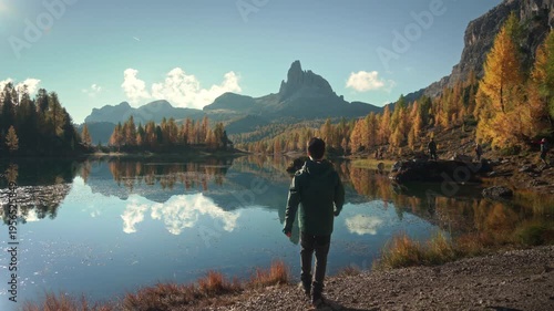 Scenic autumn landscape of male hiker visiting at Lago di Federa with Croda da Lago peak surrounded by larch forest in Dolomites, Italy
