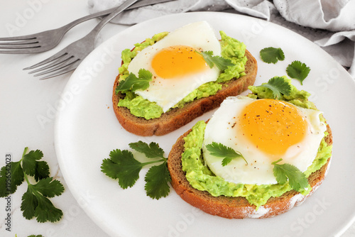 Healthy avocado toast with sunny side up fried eggs on sourdough bread. Close up on a white table background.