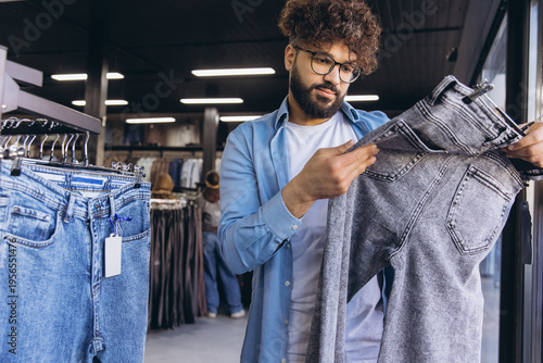 Tableau sur toile Middle Eastern man shopping for new denim jeans in a clothing store, examining f