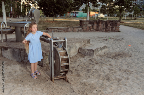 Girl standing at sandy playground water wheel