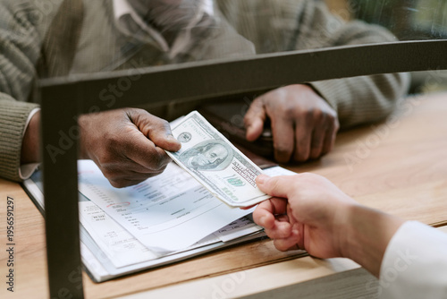 Cuadro en lienzo Middle aged Black man handing one hundred dollar bill to woman across bank count