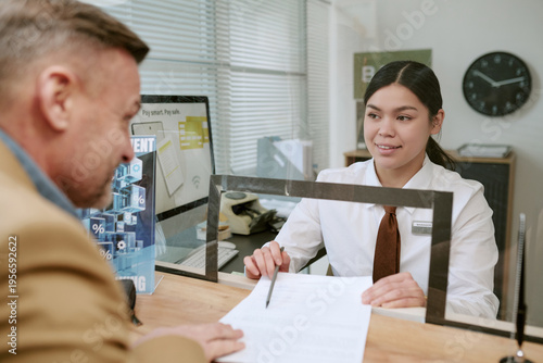 Obraz na plátně Caucasian man signing document at counter while bank employee assisting behind g