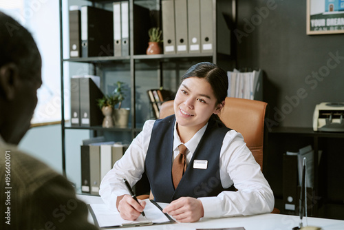 Obraz na plátně Young adult Asian woman sitting at desk assisting senior Black man with paperwor