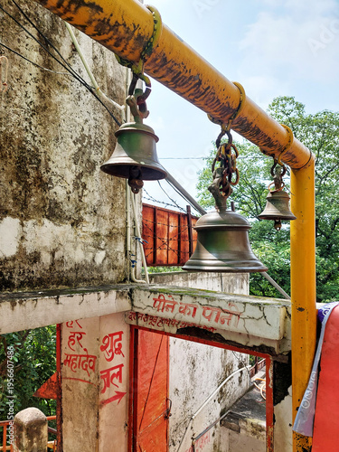 Traditional brass bells hang in a Hindu temple with walls inscribed in Sanskrit. Close-up of ghantas used to invoke deities and clear the mind before prayer. Rituals of North India.