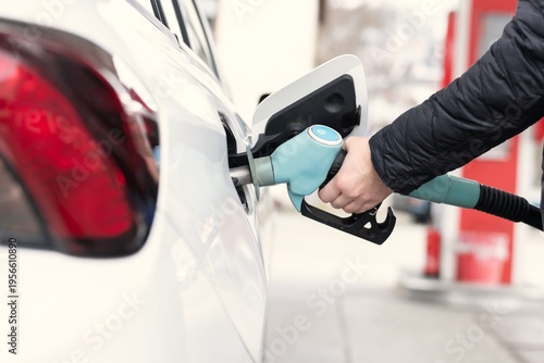 Hand holding fuel pump nozzle while refueling vehicle at station