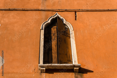 Typical ancient Venetian window with Gothic arche and dark wooden shutters and stone window sills set into an orange wall. Venice, Italy